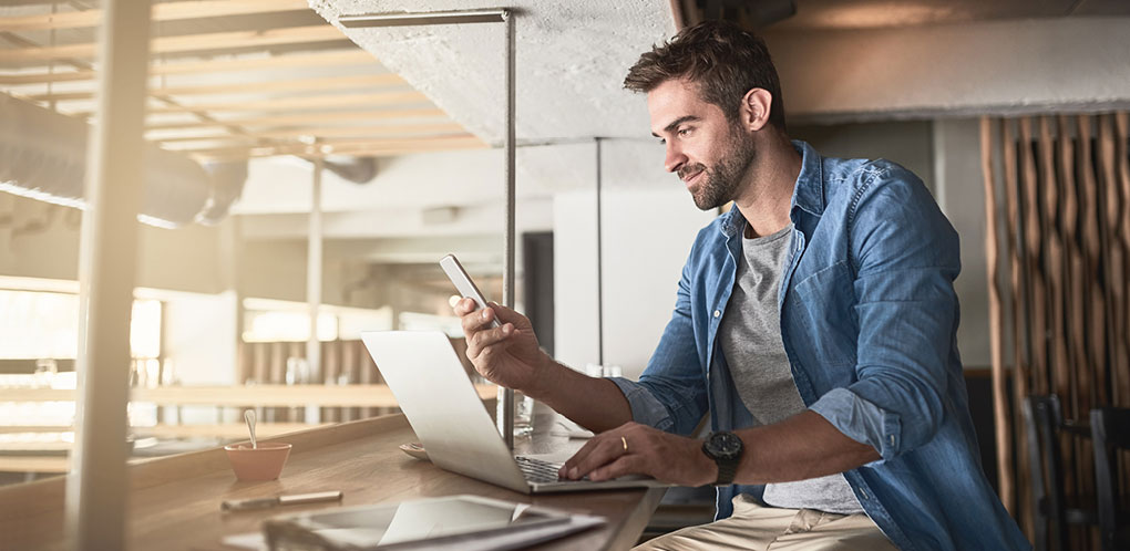 Man using phone and computer in restaurant